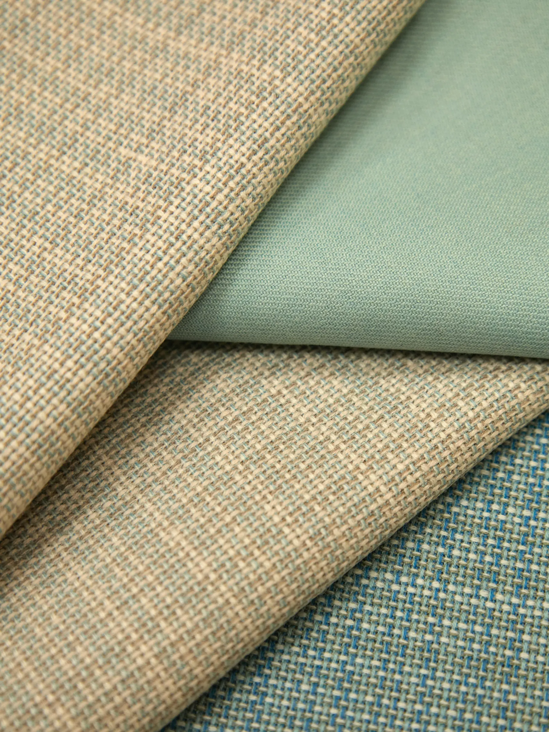 Folded fabric swatches in oatmeal tweed, sage cotton and blue basketweave overlapping on a table