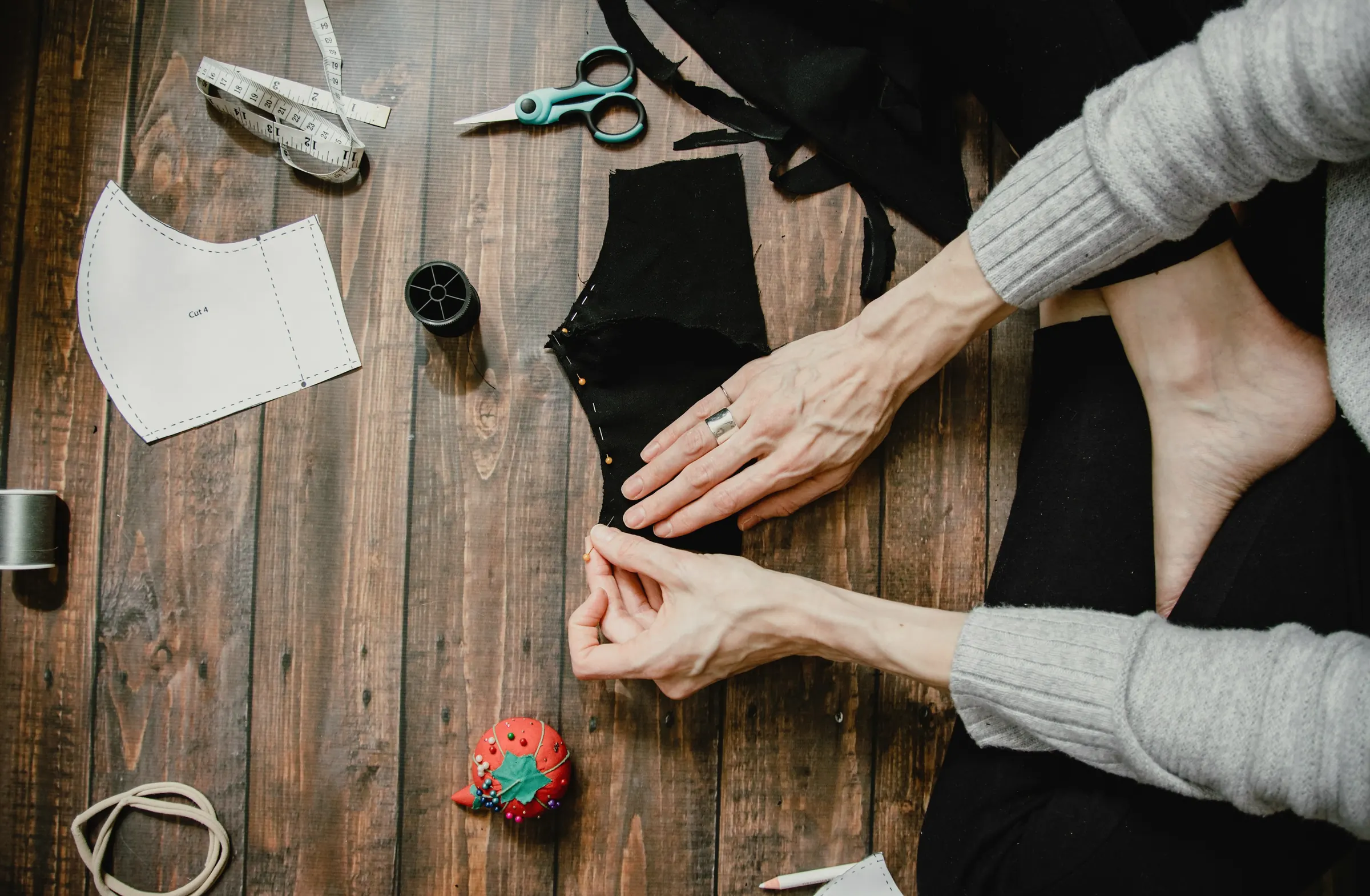 Hands laying out cut fabric pattern pieces on a dark wooden workbench beside scissors and thread