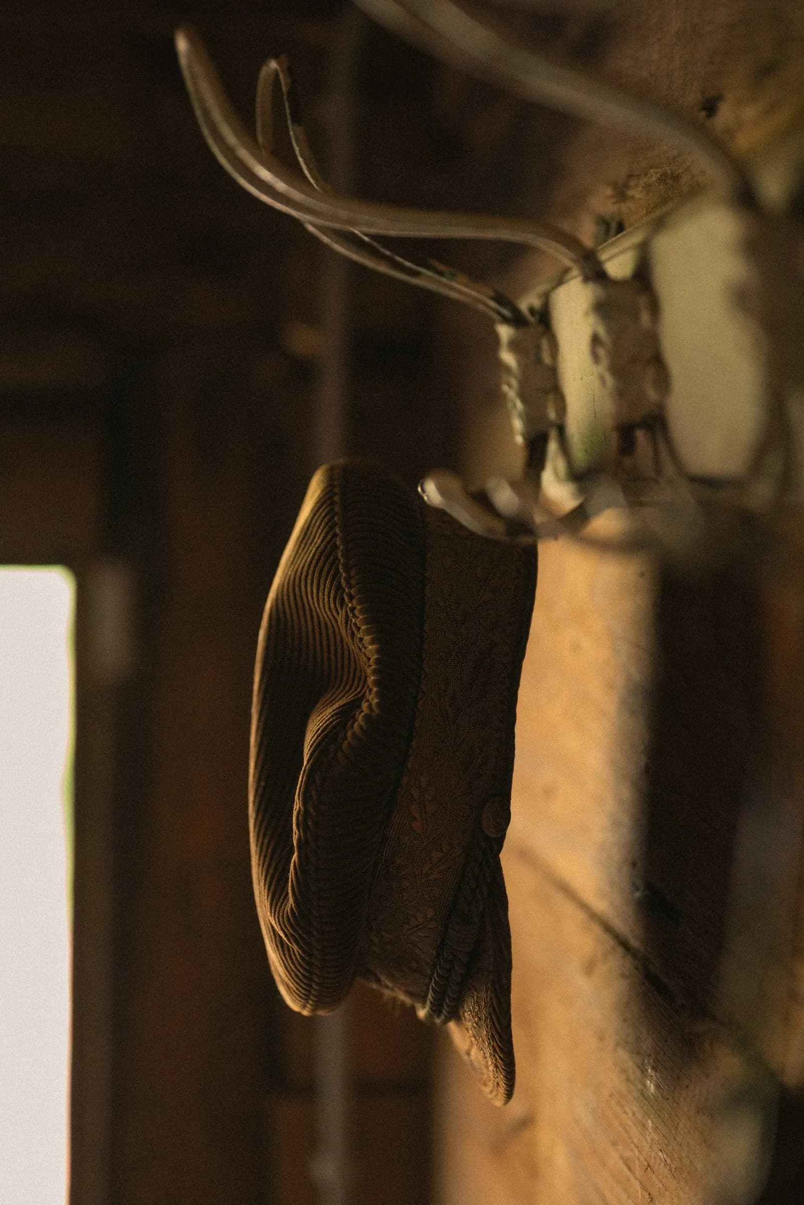 A brown corduroy cap hanging from an old iron hook on a timber wall in warm side light