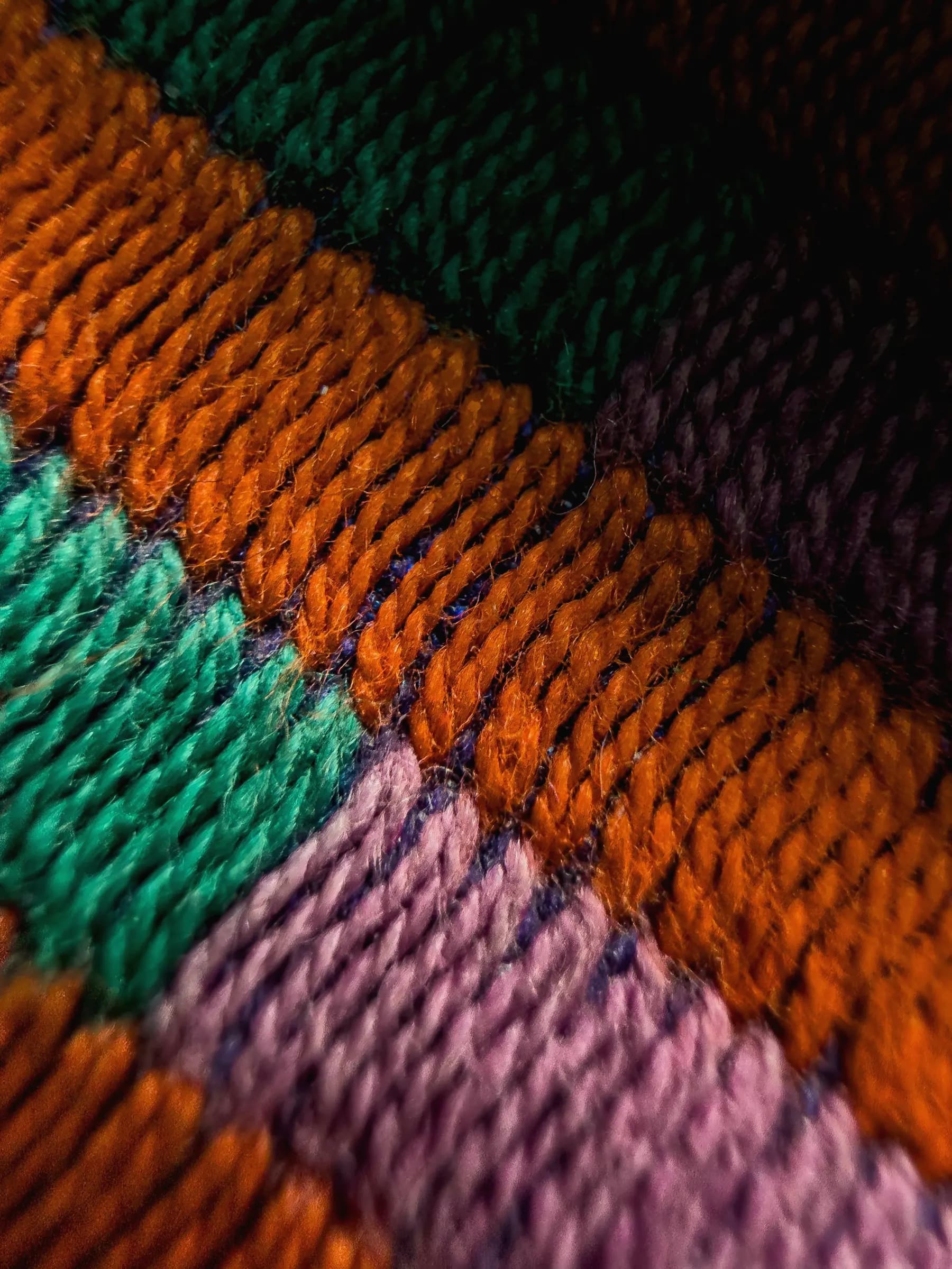 Macro of a knit in bold diagonal stripes of burnt orange, jade green, orchid pink and plum