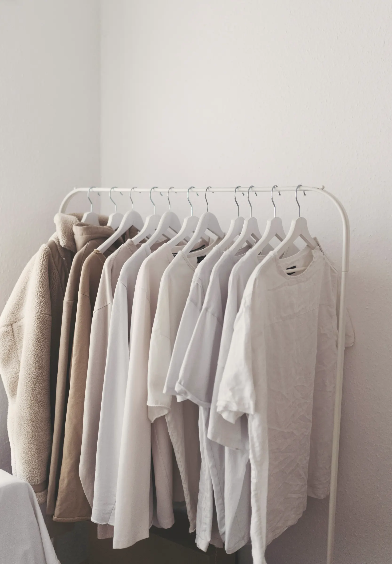 A white rail of cream, oat and white long- and short-sleeve tees on white hangers in a bright corner