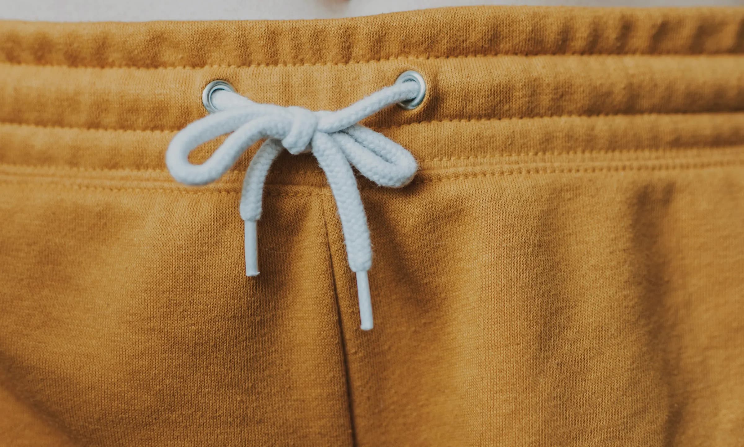 Close-up of a mustard fleece waistband with metal eyelets and a pale-blue tied drawcord